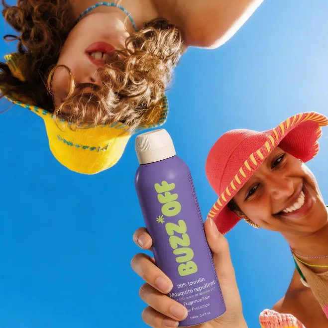 Two friends in sun hats holding a BuzzOff can, shot from below against blue sky